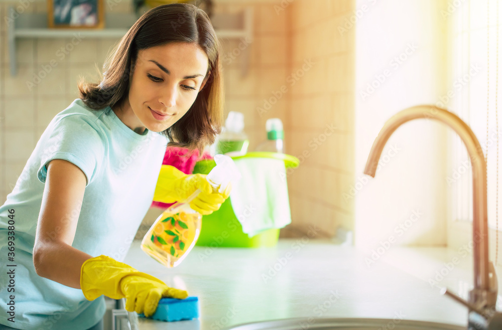 Happy beautiful young woman in yellow gloves is cleaning the kitchen with special equipment and spray. Housework and cleaning stuff Happy beautiful young woman in yellow gloves is cleaning the kitchen with special equipment and spray. Housework and cleaning stuff