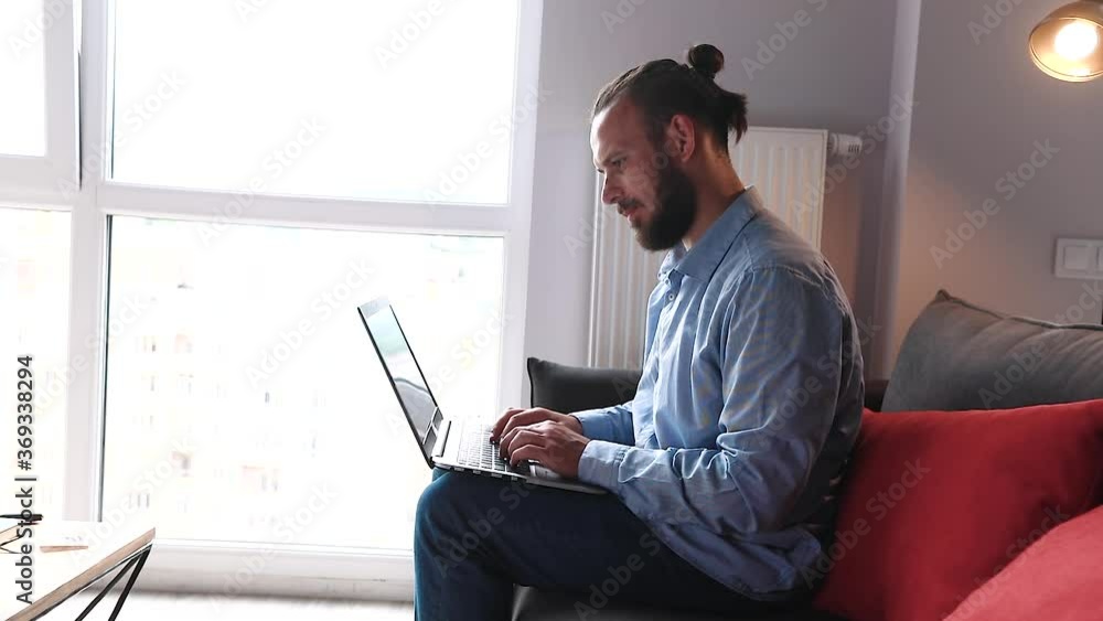 young hispanic guy sitting on the couch and typing a message on a laptop young hispanic guy sitting on the couch and typing a message on a laptop