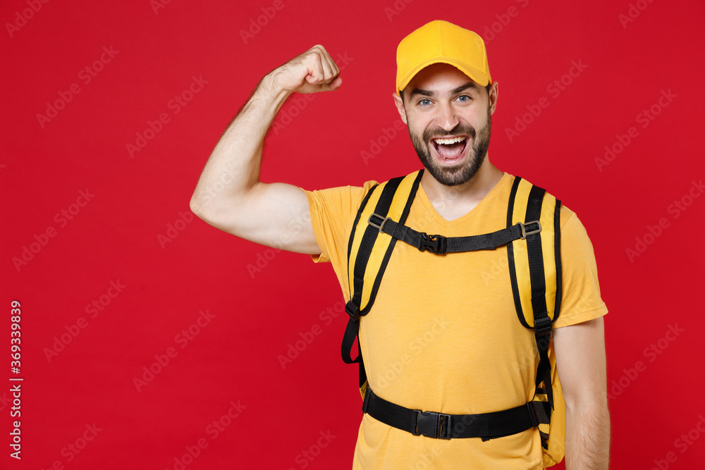 Delivery employee man guy male 20s in yellow cap t-shirt uniform thermal bag backpack with food work as courier isolated on red background studio. Service during quarantine coronavirus covid-19 virus.