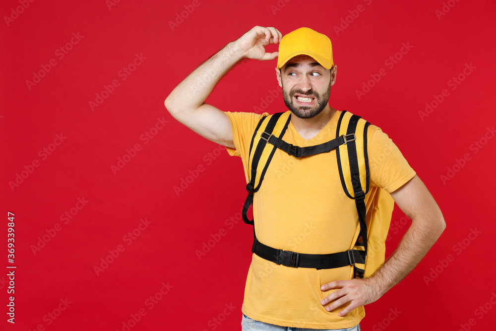 Sad delivery employee man guy 20s in yellow cap t-shirt uniform thermal bag backpack with food work as courier isolated on red background studio. Service during quarantine coronavirus covid-19 virus.