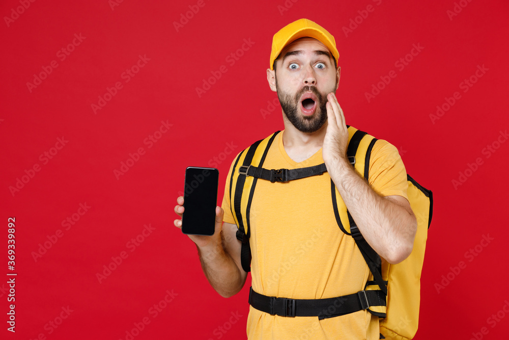 Delivery man in yellow cap t-shirt uniform thermal bag backpack with food hold cellphone isolated on red background studio Guy male employee work as courier Service coronavirus covid-19 virus concept Delivery man in yellow cap t-shirt uniform thermal bag backpack with food hold cellphone isolated on red background studio Guy male employee work as courier Service coronavirus covid-19 virus concept