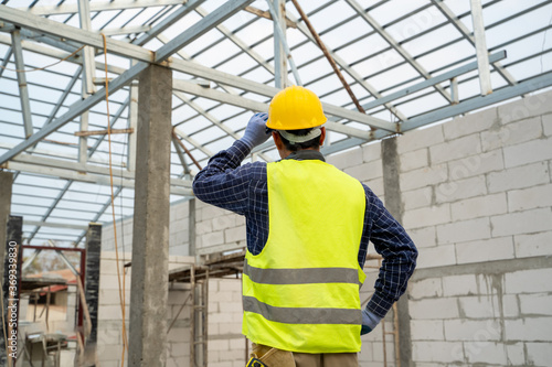 Construction engineer wearing safety vest and yellow helmet working at house building site,House construction concept.