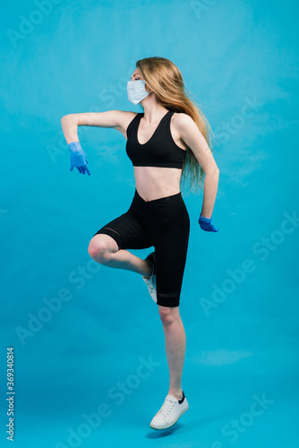 Fitness girl wearing medicine mask in fitness costume isolated on blue background. Training during quarantine, covid 19, coronavirus.