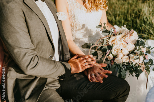 Closeup of bride and groom sitting together on outdoor wedding ceremony with fresh floral bouquet and rings. Horizontal avaible light color photography. photo