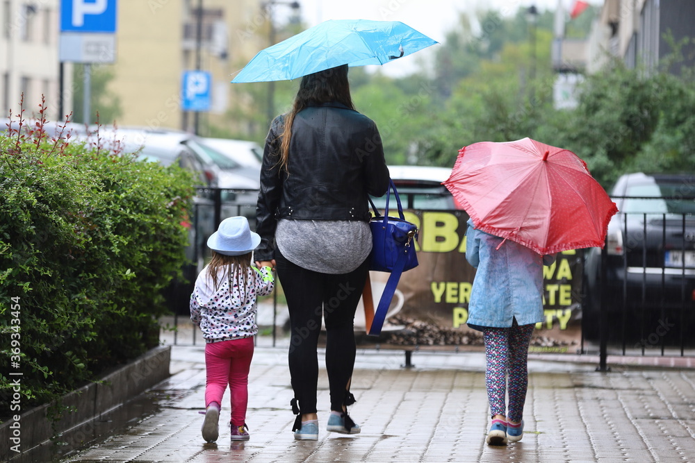 Φωτογραφία a woman with children cross the street with an umbrella in the rain