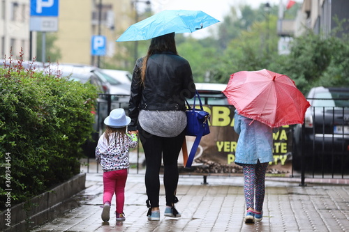 a woman with children cross the street with an umbrella in the rain