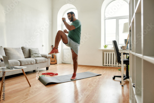 Get Fit. Full length shot of young active man watching online video training on laptop, exercising during morning workout at home. Sport, healthy lifestyle
