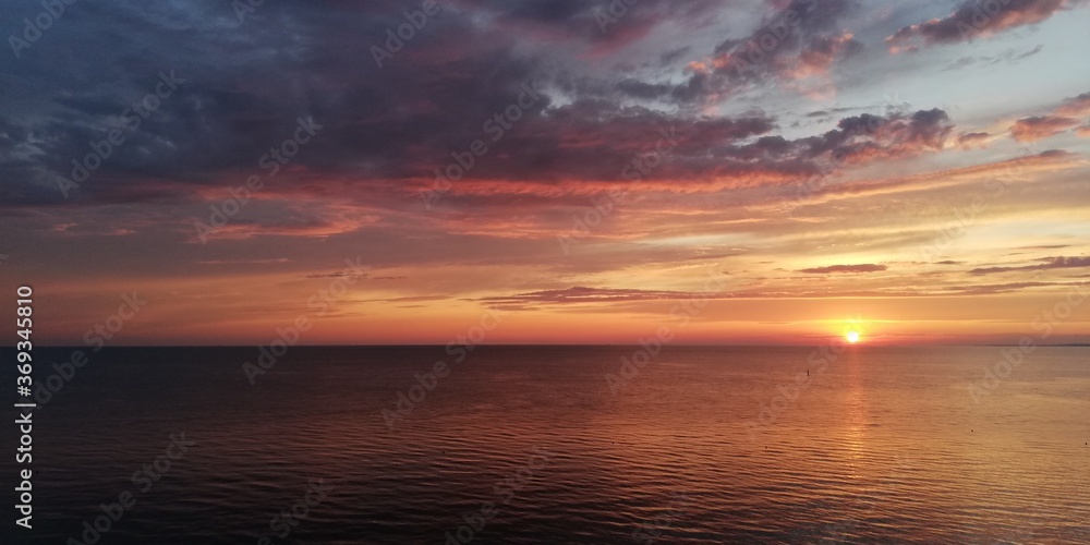 Fototapeta premium Bright dramatic sea sunset landscape in golden and grey colors. Autumn sunset in the sky of amazing beauty.The sea horizon is hidden in a dark haze. Halloween background 