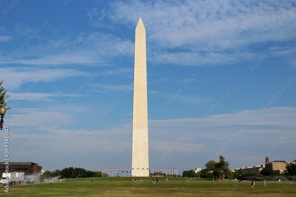 Obelisk, the Washington Monument, at the National Mall surrounded by American Flags on a sunny day with blue sky