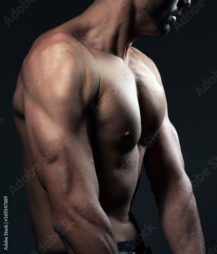  Shirtless young man isolated on dark background. Studio shot.