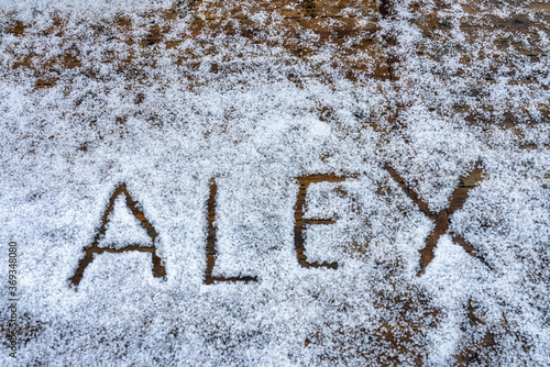 Close up at name Alex which is written is in capital letters on hail stones at wooden terrace during hailstorm from sky with sunlight