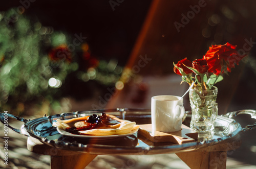 Still life shot of breakfast tray silver platter with cup of coffee, roses and pancakes bathed in golden light with lens flare