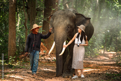 Asian woman walking with elephant and mahout in the forest. Tourism asian women holding camera in elephant village. © Thirawatana