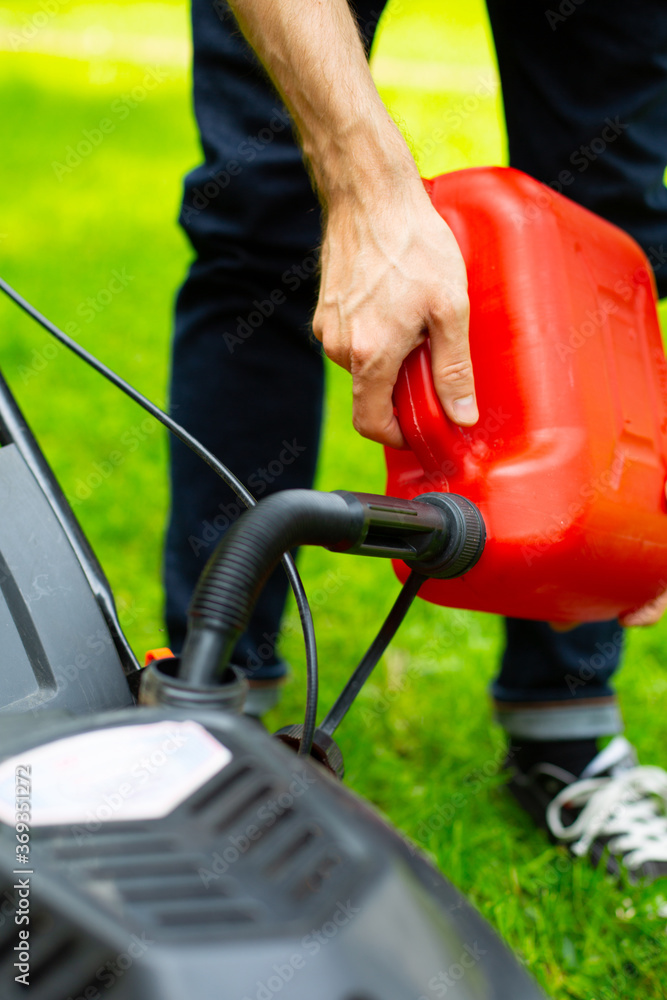 Refilling the fuel tank in a petrol lawn mower. Gardening, mowing with a gasoline lawnmower.