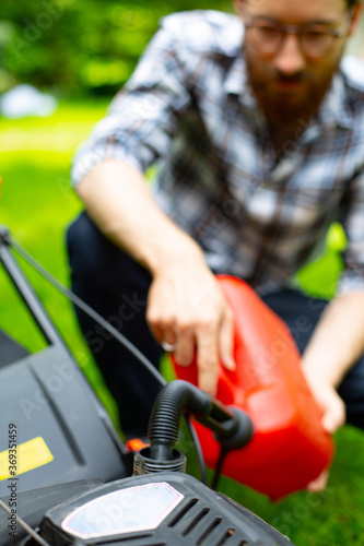 Refilling the fuel tank in a petrol lawn mower. Gardening, mowing with a gasoline lawnmower. © JacZia