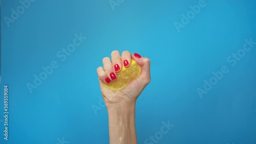 Slow Motion squeeze juice from lemon, close up woman hand squeezes half yellow lemon on blue background. Exhausted.