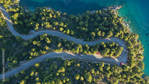 Aerial top down photo of snake road covered in pine trees leading to famous and picturesque small fishing village of Agnontas, Skopelos island, Sporades, Greece