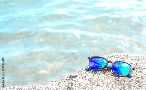 Close up of sand and sunglasses with blurred sea background.