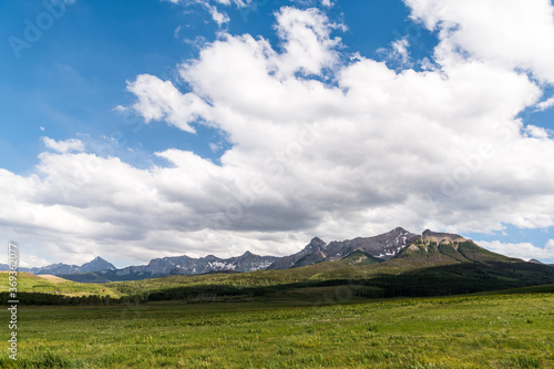 Typical landscape scene in the western USA of open ranchland with lush green, grassy fields beneath a snow-capped mountain range