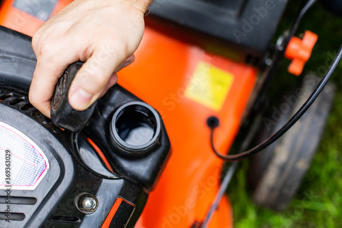 Refilling the fuel tank in a petrol lawn mower, close up on an open fuel filler. Gardening with a gasoline lawnmower.