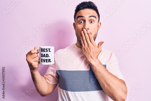 Canvas-taulu Young handsome man with beard drinking mug of coffee with best dad ever message covering mouth with hand, shocked and afraid for mistake