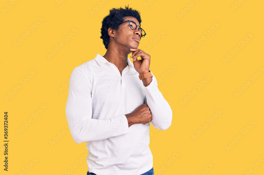 Handsome african american man with afro hair wearing casual clothes and glasses with hand on chin thinking about question, pensive expression. smiling with thoughtful face. doubt concept. Handsome african american man with afro hair wearing casual clothes and glasses with hand on chin thinking about question, pensive expression. smiling with thoughtful face. doubt concept.