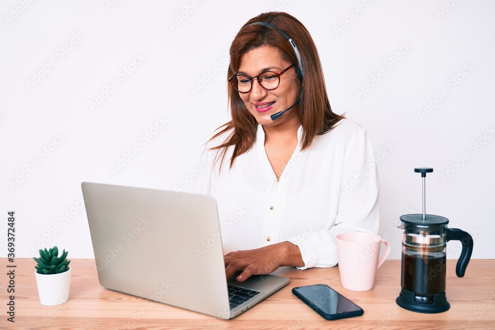 Middle age brunette hispanic woman working at the office wearing operator headset looking positive and happy standing and smiling with a confident smile showing teeth Middle age brunette hispanic woman working at the office wearing operator headset looking positive and happy standing and smiling with a confident smile showing teeth