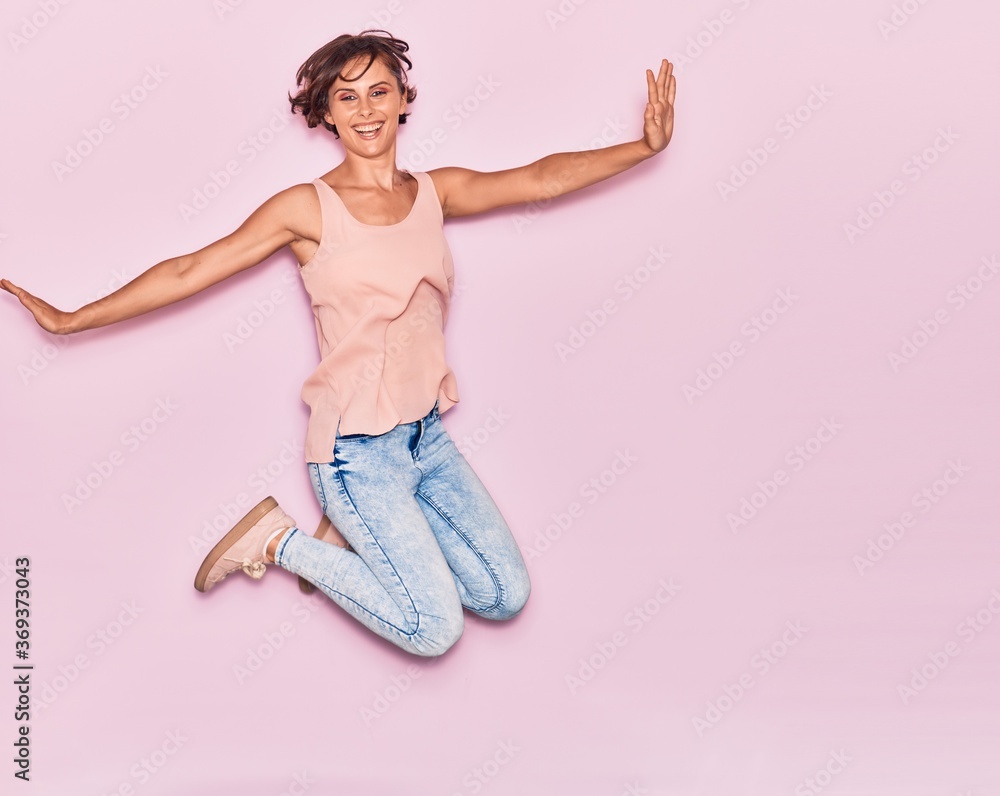 Young beautiful woman wearing casual clothes smiling happy. Jumping with smile on face and arms opened over isolated pink background. Young beautiful woman wearing casual clothes smiling happy. Jumping with smile on face and arms opened over isolated pink background.