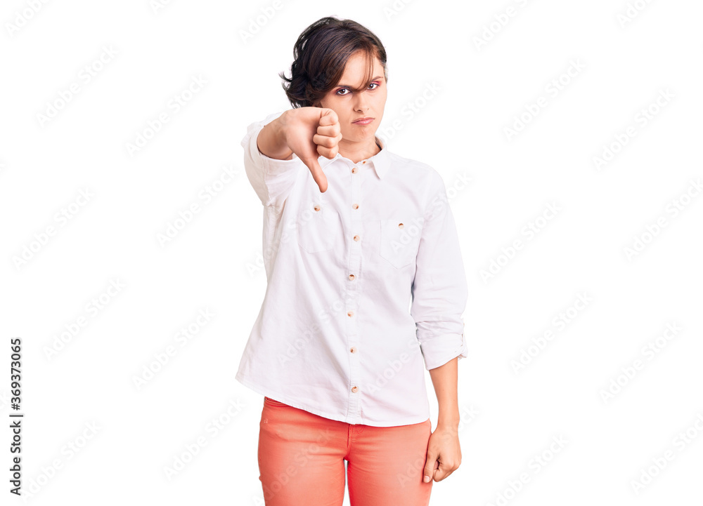 Beautiful young woman with short hair wearing elegant white shirt looking unhappy and angry showing rejection and negative with thumbs down gesture. bad expression. Beautiful young woman with short hair wearing elegant white shirt looking unhappy and angry showing rejection and negative with thumbs down gesture. bad expression.