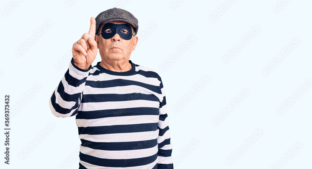 Senior handsome man wearing burglar mask and t-shirt pointing with finger up and angry expression, showing no gesture Senior handsome man wearing burglar mask and t-shirt pointing with finger up and angry expression, showing no gesture