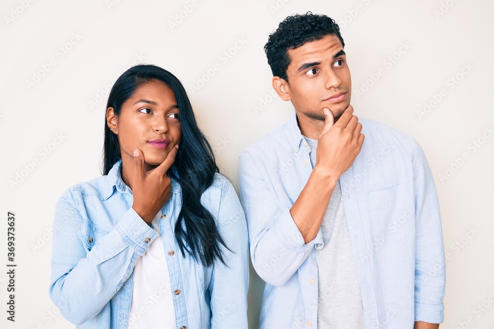 Beautiful latin young couple wearing casual clothes with hand on chin thinking about question, pensive expression. smiling with thoughtful face. doubt concept. Beautiful latin young couple wearing casual clothes with hand on chin thinking about question, pensive expression. smiling with thoughtful face. doubt concept.