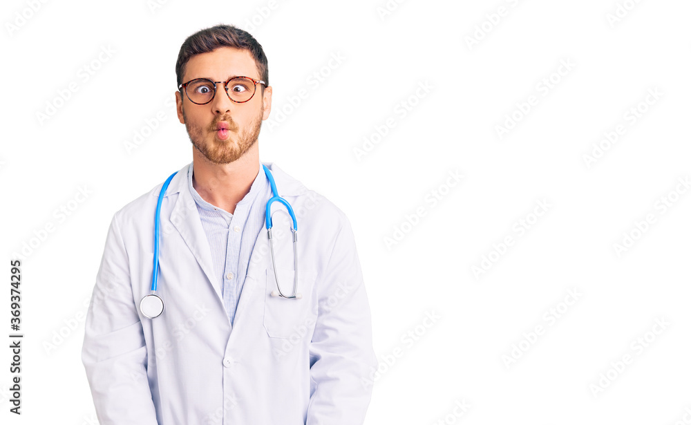 Handsome young man with bear wearing doctor uniform making fish face with lips, crazy and comical gesture. funny expression.