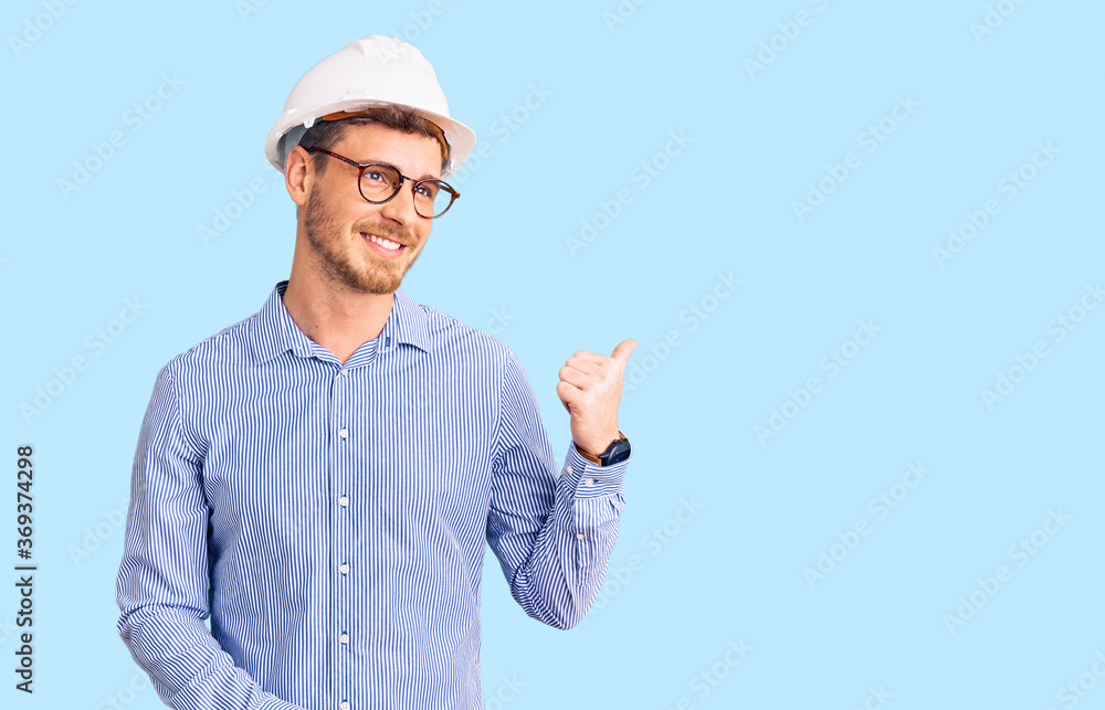 Handsome young man with bear wearing architect hardhat smiling with happy face looking and pointing to the side with thumb up. Handsome young man with bear wearing architect hardhat smiling with happy face looking and pointing to the side with thumb up.