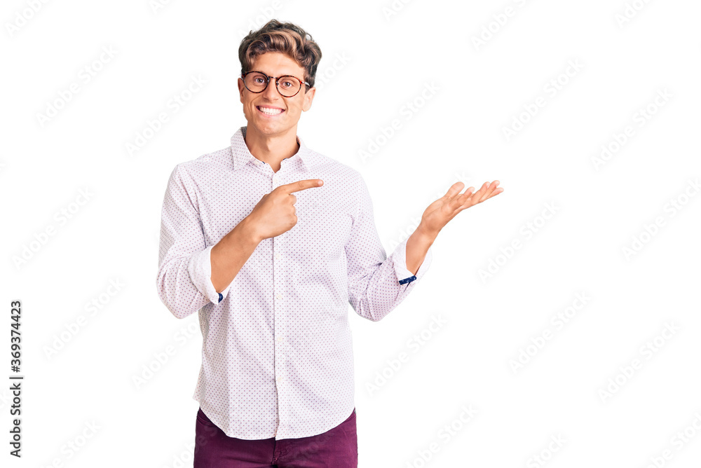Young handsome man wearing business clothes and glasses amazed and smiling to the camera while presenting with hand and pointing with finger. Young handsome man wearing business clothes and glasses amazed and smiling to the camera while presenting with hand and pointing with finger.