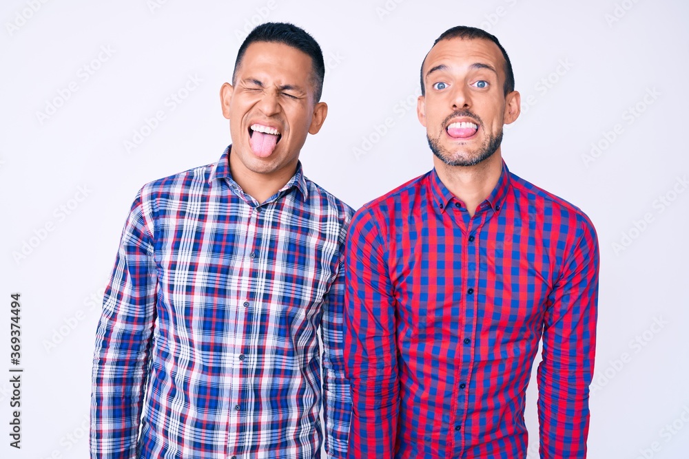 Young gay couple of two men wearing casual clothes sticking tongue out happy with funny expression. emotion concept.