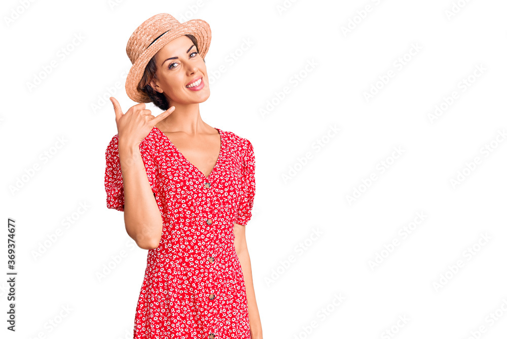 Young beautiful woman wearing summer hat smiling doing phone gesture with hand and fingers like talking on the telephone. communicating concepts. Young beautiful woman wearing summer hat smiling doing phone gesture with hand and fingers like talking on the telephone. communicating concepts.