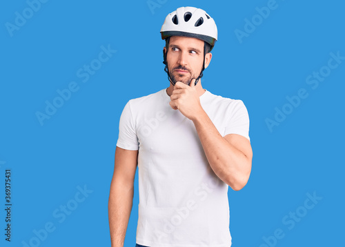 Young handsome man wearing bike helmet with hand on chin thinking about question, pensive expression. smiling with thoughtful face. doubt concept.