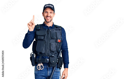 Young handsome man wearing police uniform pointing finger up with successful idea. exited and happy. number one.