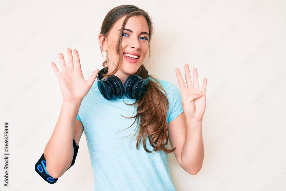 Beautiful young caucasian woman wearing gym clothes and using headphones showing and pointing up with fingers number nine while smiling confident and happy. Beautiful young caucasian woman wearing gym clothes and using headphones showing and pointing up with fingers number nine while smiling confident and happy.