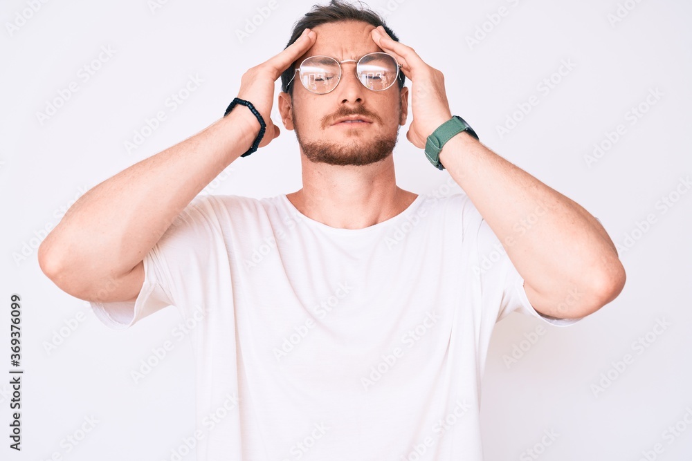 Young handsome man wearing casual clothes and glasses with hand on head, headache because stress. suffering migraine. Young handsome man wearing casual clothes and glasses with hand on head, headache because stress. suffering migraine.