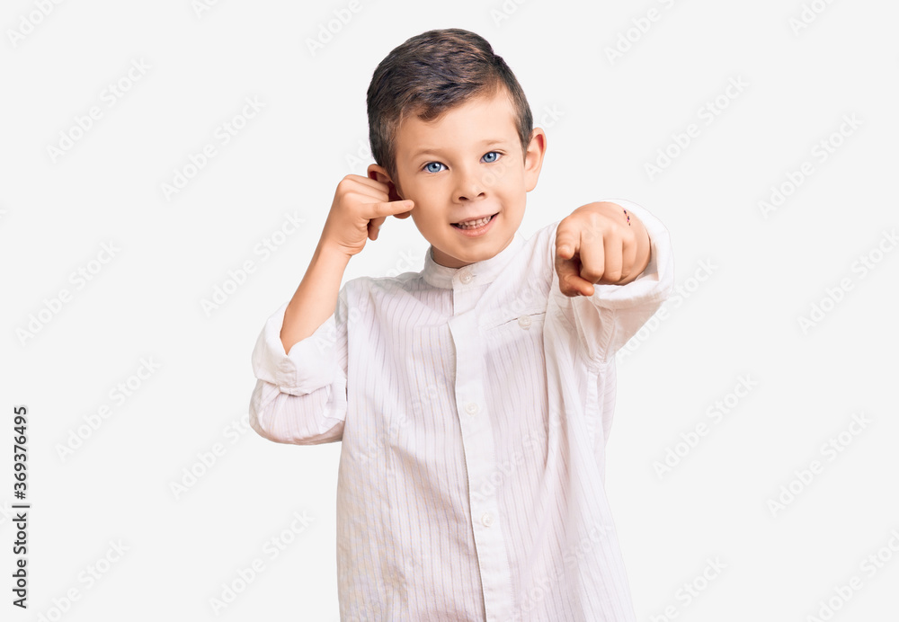 Cute blond kid wearing elegant shirt smiling doing talking on the telephone gesture and pointing to you. call me. Cute blond kid wearing elegant shirt smiling doing talking on the telephone gesture and pointing to you. call me.