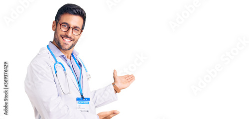 Obraz na płótnie Young hispanic man wearing doctor uniform and stethoscope inviting to enter smil