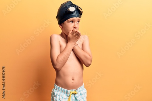 Cute blond kid wearing swimwear and swimmer glasses looking stressed and nervous with hands on mouth biting nails. anxiety problem. © Krakenimages.com