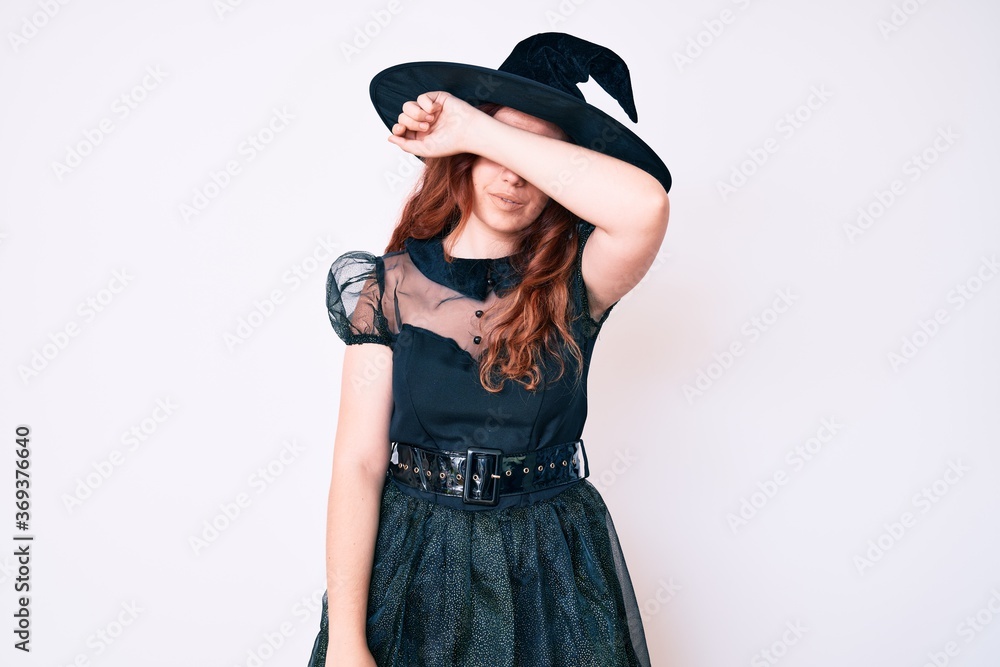 Young beautiful woman wearing witch halloween costume covering eyes with arm, looking serious and sad. sightless, hiding and rejection concept