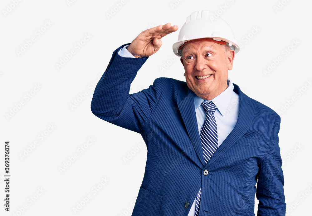 Senior handsome grey-haired man wearing suit and architect hardhat very happy and smiling looking far away with hand over head. searching concept. Senior handsome grey-haired man wearing suit and architect hardhat very happy and smiling looking far away with hand over head. searching concept.