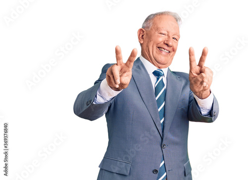 Senior handsome grey-haired man wearing elegant suit smiling looking to the camera showing fingers doing victory sign. number two.