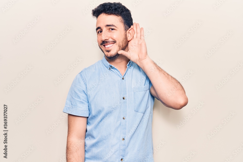 Young hispanic man wearing casual clothes smiling with hand over ear listening and hearing to rumor or gossip. deafness concept. Young hispanic man wearing casual clothes smiling with hand over ear listening and hearing to rumor or gossip. deafness concept.