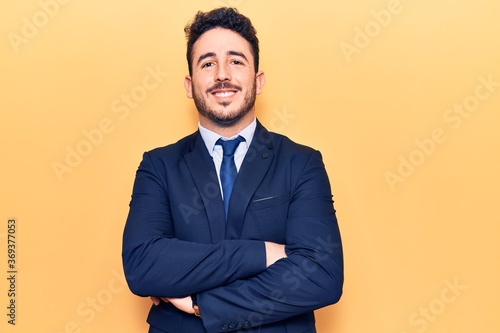 Young hispanic man wearing suit happy face smiling with crossed arms looking at the camera. positive person.