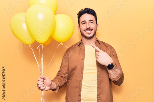 Young hispanic man holding balloons smiling happy pointing with hand and finger