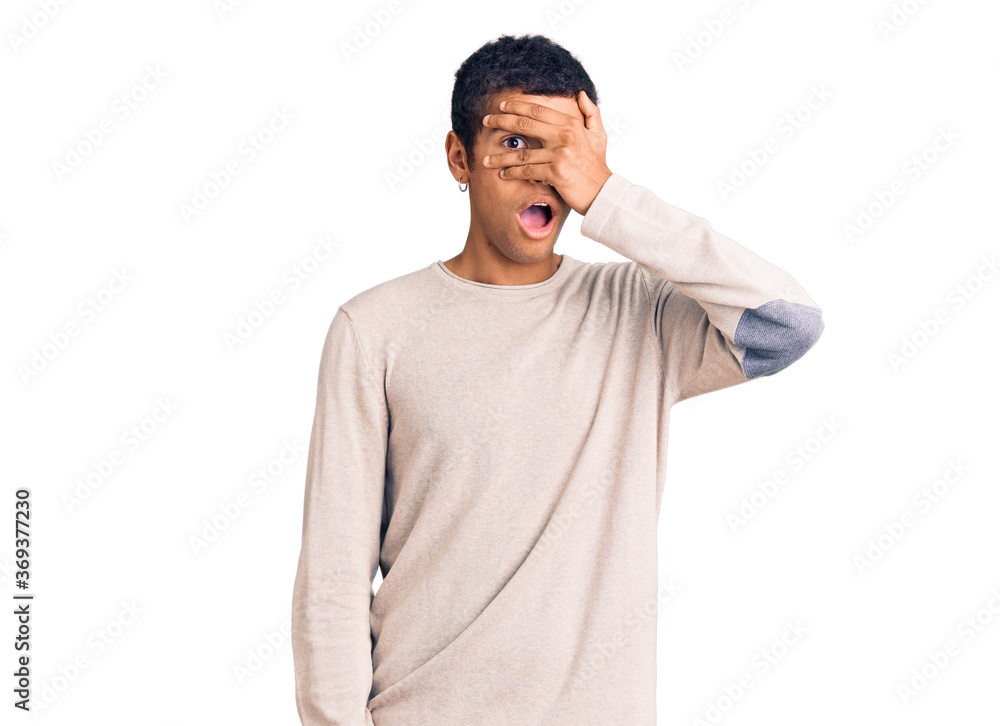 Fototapeta premium Young african amercian man wearing casual clothes peeking in shock covering face and eyes with hand, looking through fingers with embarrassed expression.